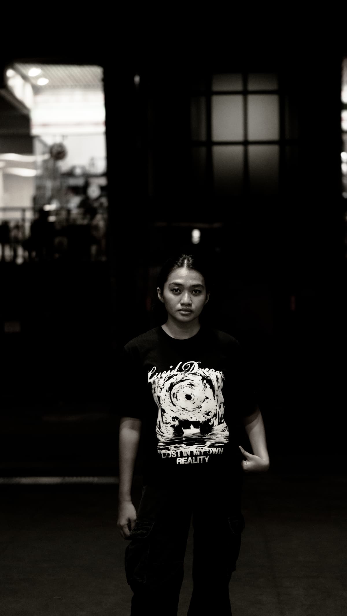 A model in the LD Signature Shirt in Black, facing the camera in front of a lit window at night